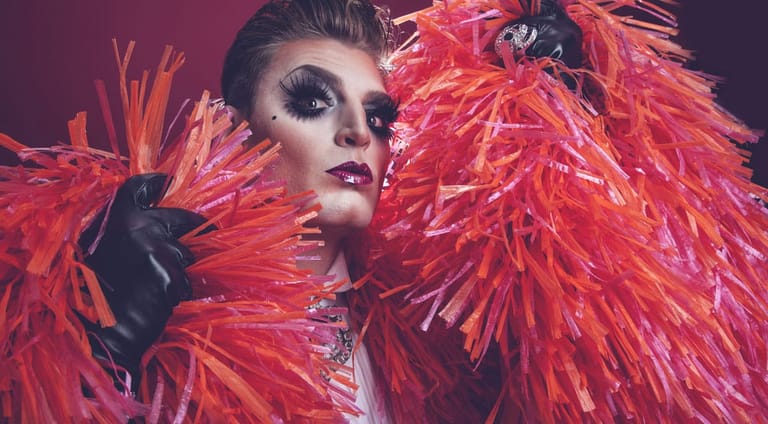 Performer in bold red feathered costume and dramatic makeup against a dark purple background.