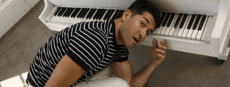 Performer in a striped shirt poses playfully beside a white keyboard against a concrete floor.