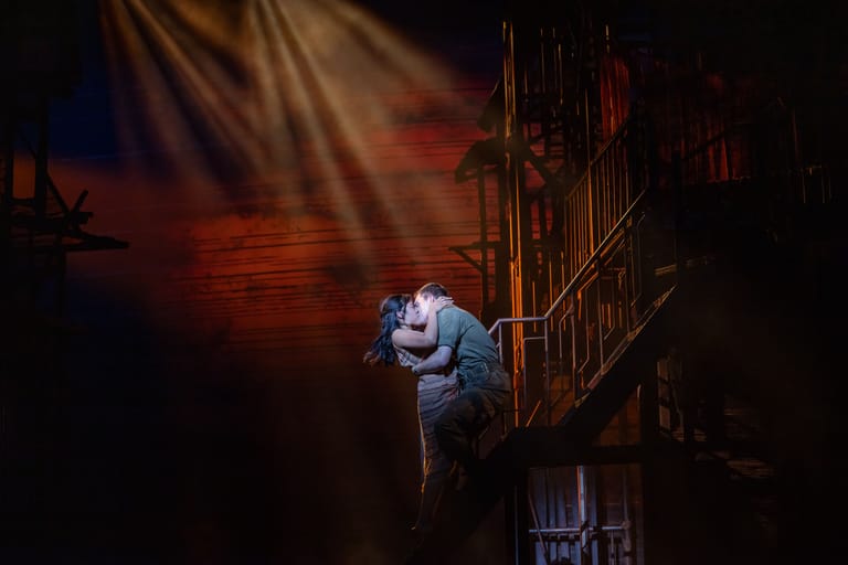 Performer suspended above a gothic stage set beneath warm amber lighting during a theatrical production.