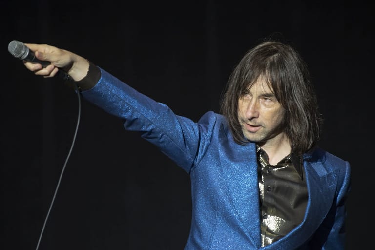 Performer in a blue jacket singing into a microphone with arm extended during a stage performance.