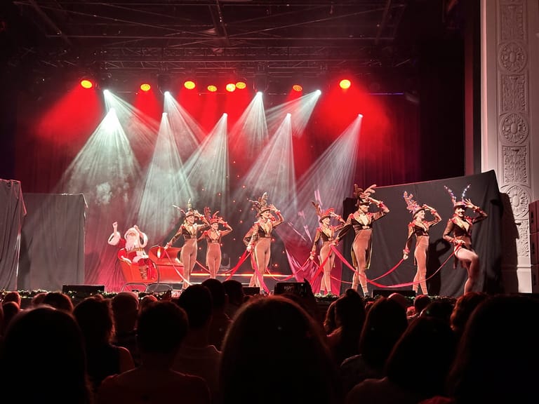 Performers in red costumes dance on stage beneath dramatic red and white lighting during The Christmas Spectacular.