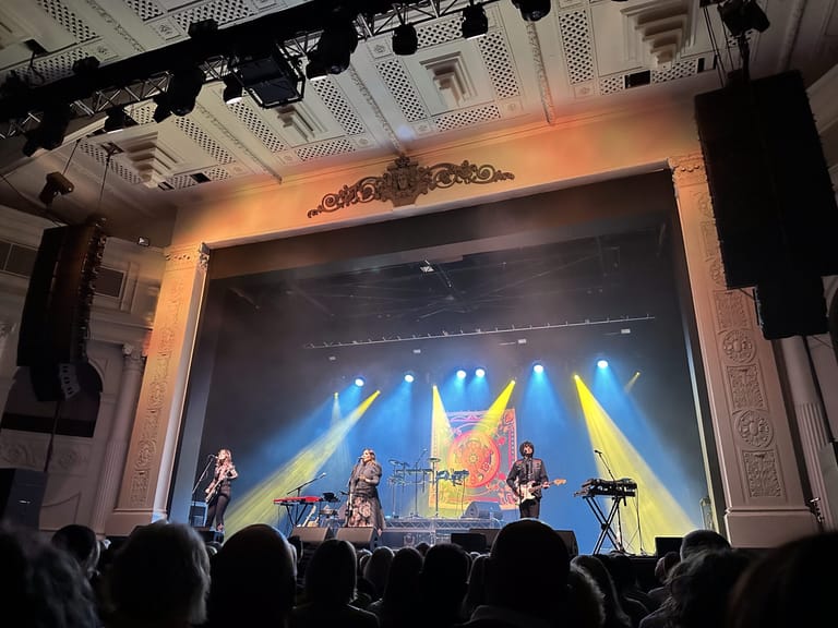 Singer and band members performing on stage bathed in blue and yellow spotlight beams in a theatre venue.