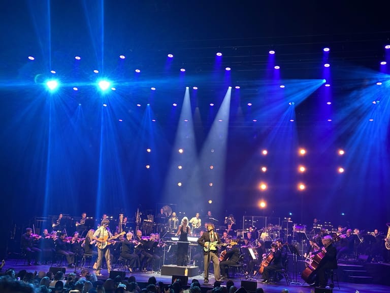 Lime Cordiale performs with Adelaide Symphony Orchestra on an illuminated stage beneath dramatic blue and purple lighting.