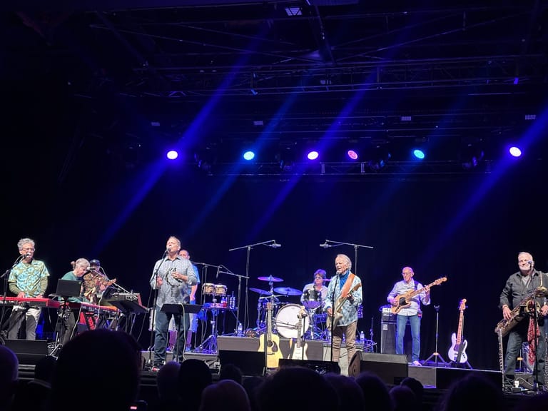 Band members perform on stage under blue spotlights during Al Jardine & The Pet Sounds Band concert.
