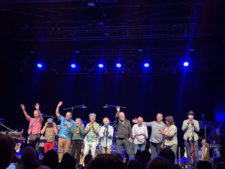 Large band ensemble taking a bow on stage under blue spotlights during a concert performance.
