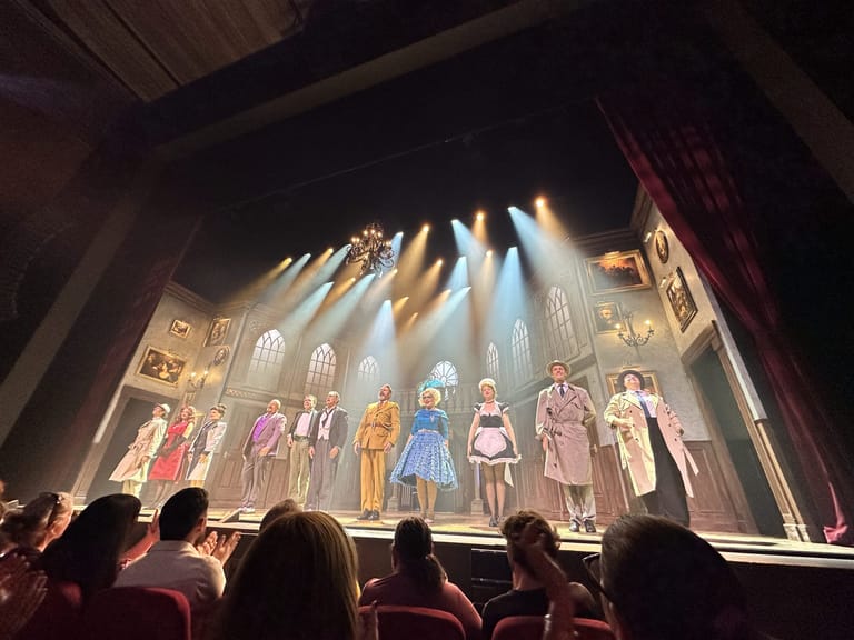 Cast members in period costumes stand illuminated by dramatic stage lighting during a Cluedo theatre production.