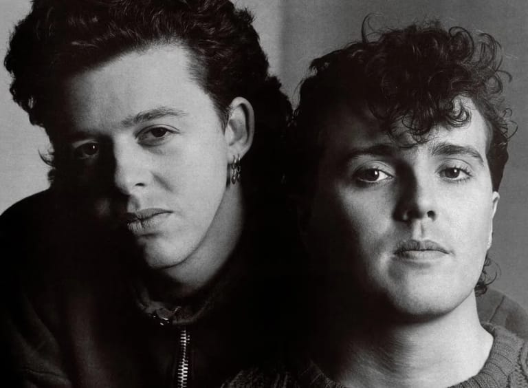 Two men pose together for a black and white portrait photograph against a neutral background.