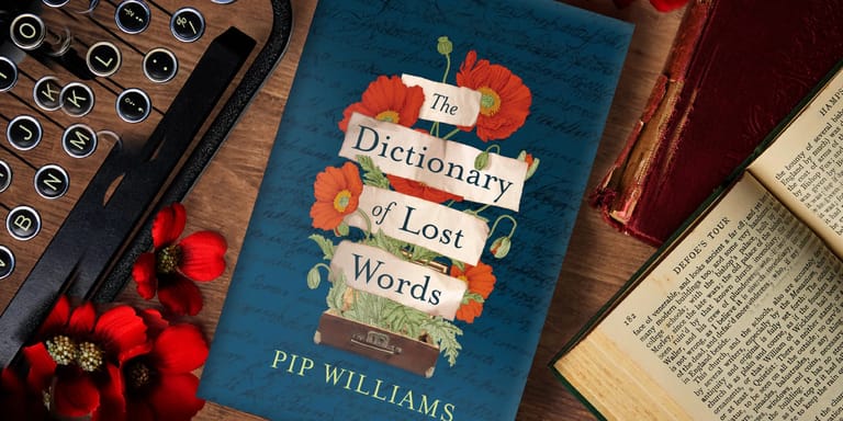 The Dictionary of Lost Words" book by Pip Williams displayed among strawberries and open pages on a wooden surface.