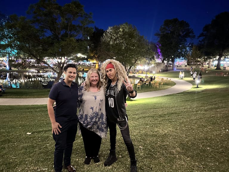Three performers stand together on an illuminated park lawn at night during an outdoor festival event.