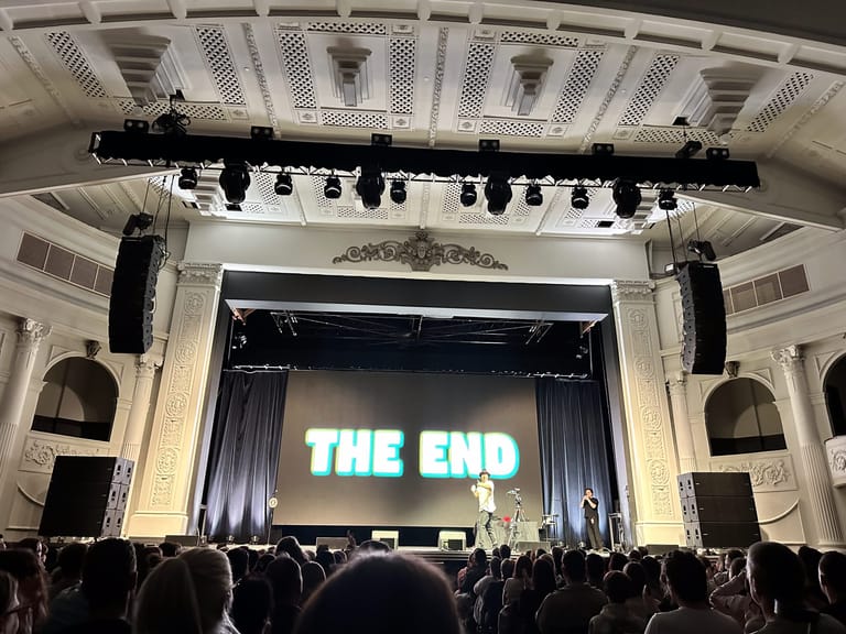 Theatre stage with "THE END" displayed on screen above audience silhouettes during Jimmy Rees performance.
