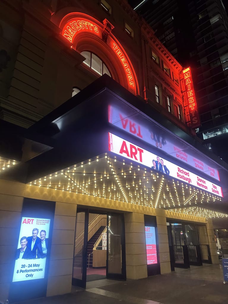 Theatre marquee illuminated with red neon signage reading "ART" and warm white lights framing the entrance below.