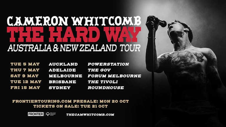 Cameron Whitcomb holds a microphone against his chest in black and white, promoting his Australia and New Zealand tour.