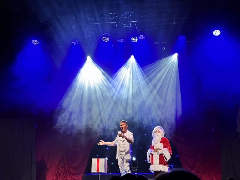Two performers on stage bathed in dramatic blue and white spotlight beams during a Christmas theatre production.