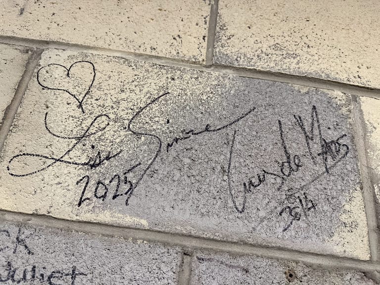 Handwritten signatures and a heart drawn on a concrete pavement stone dated 2024.