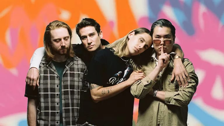 Four band members pose together against a vibrant orange and pink gradient backdrop.