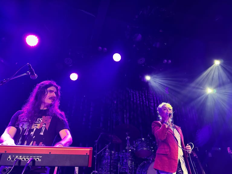 Keyboardist and singer perform under purple stage lighting during a theatrical production.