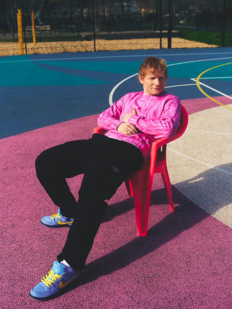 Person in pink jacket seated on red chair on colourful outdoor sports court.
