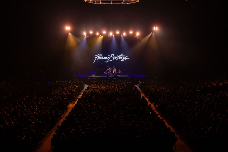 Large crowd facing an illuminated stage with "Pierce Brothers" branding and suspended lighting rig overhead.