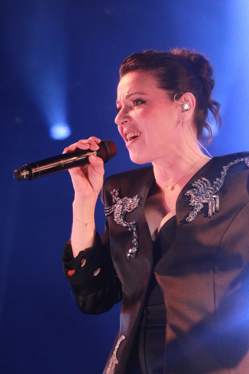 Singer performing with microphone on stage, illuminated by blue spotlight lighting.