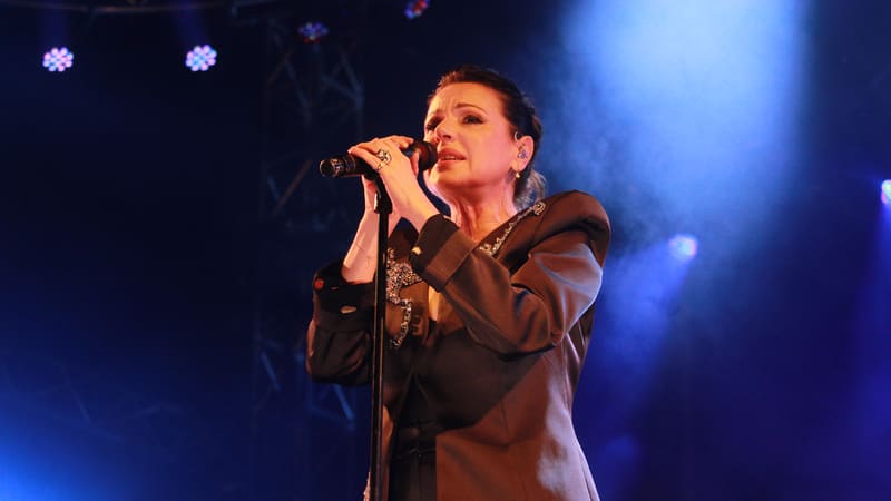 Female performer singing at microphone under blue stage lighting during a concert performance.