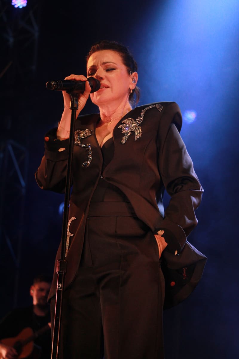 Singer performing at microphone in black embellished jacket under blue stage lighting.