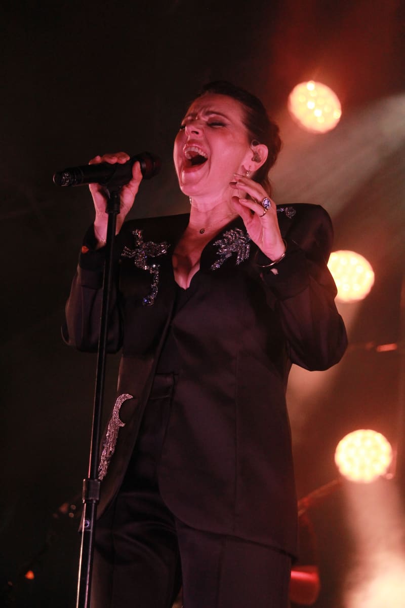 Singer in black sequinned jacket performing at microphone under warm stage spotlights.