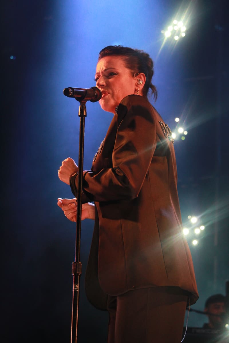 Performer in a burgundy suit singing at a microphone under blue stage lighting.