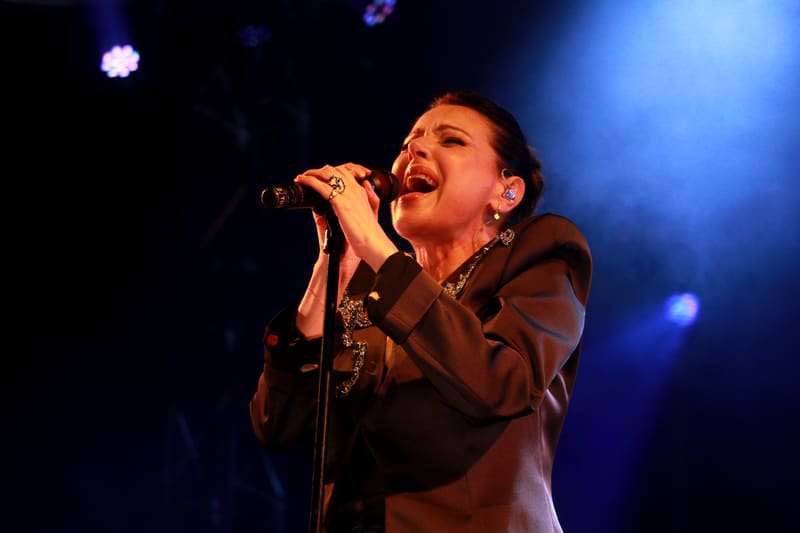 Singer performing at a microphone under blue stage lighting.