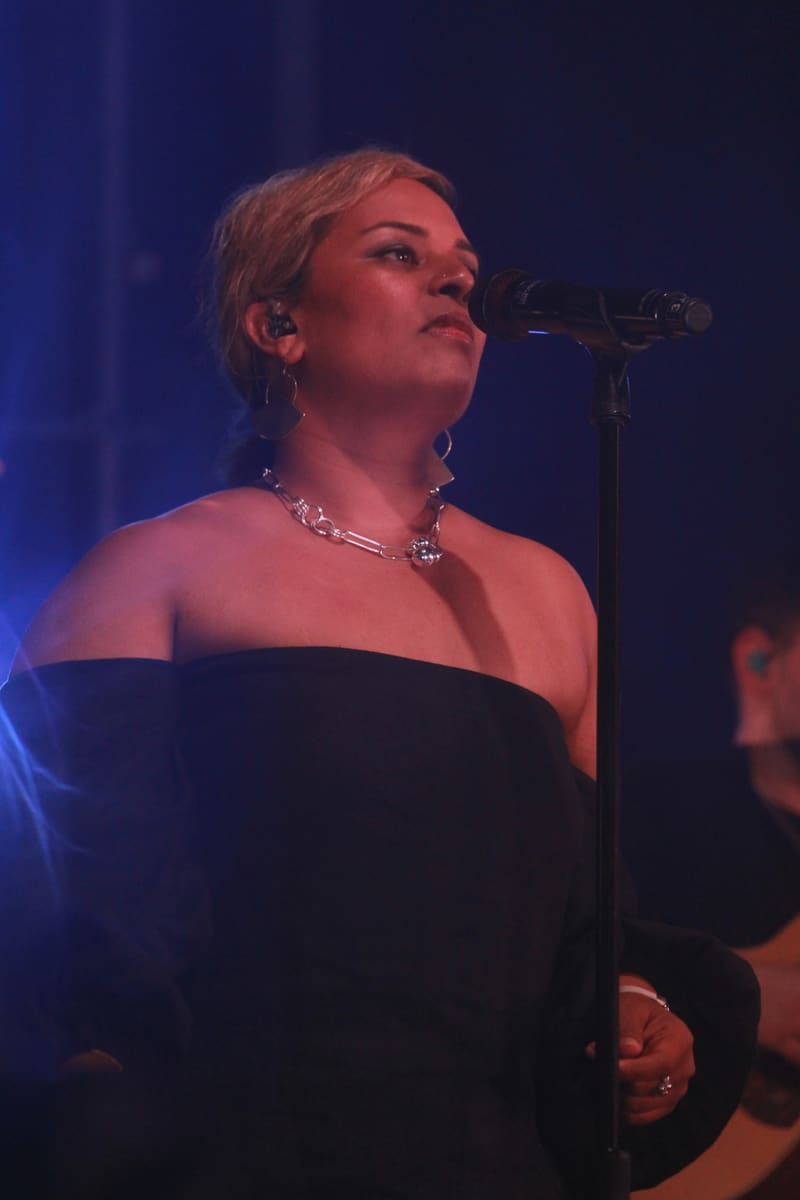 Singer performing at a microphone in a black off-shoulder dress, bathed in blue stage lighting.