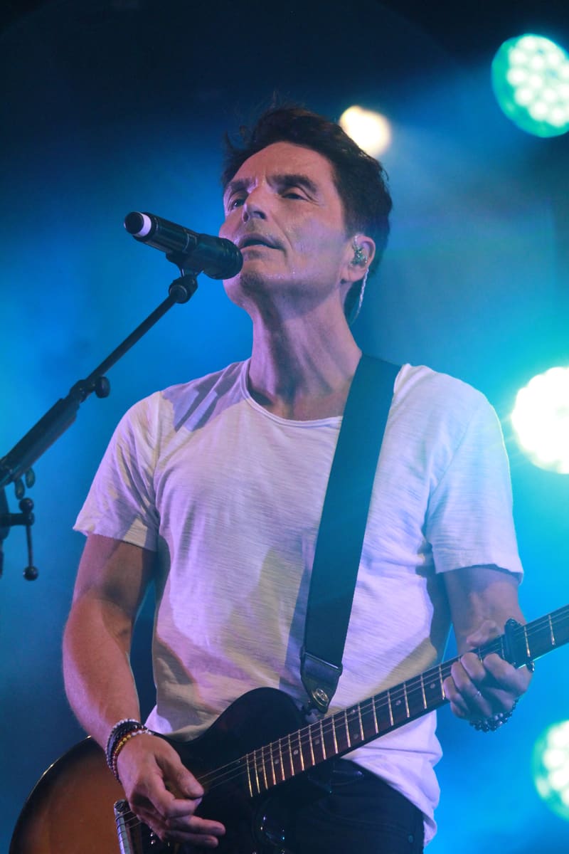 Musician performing with electric guitar at microphone under blue stage lighting.