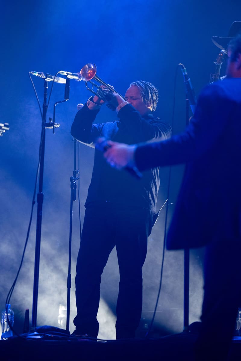 Trombonist performs on stage bathed in blue lighting during a live concert performance.