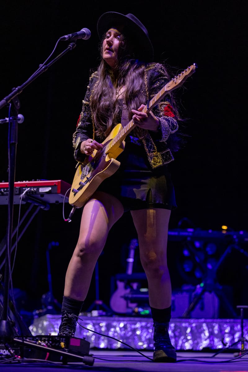 Guitarist performing with acoustic guitar at microphone under purple stage lighting during The Corrs 2023 Australian Tour.