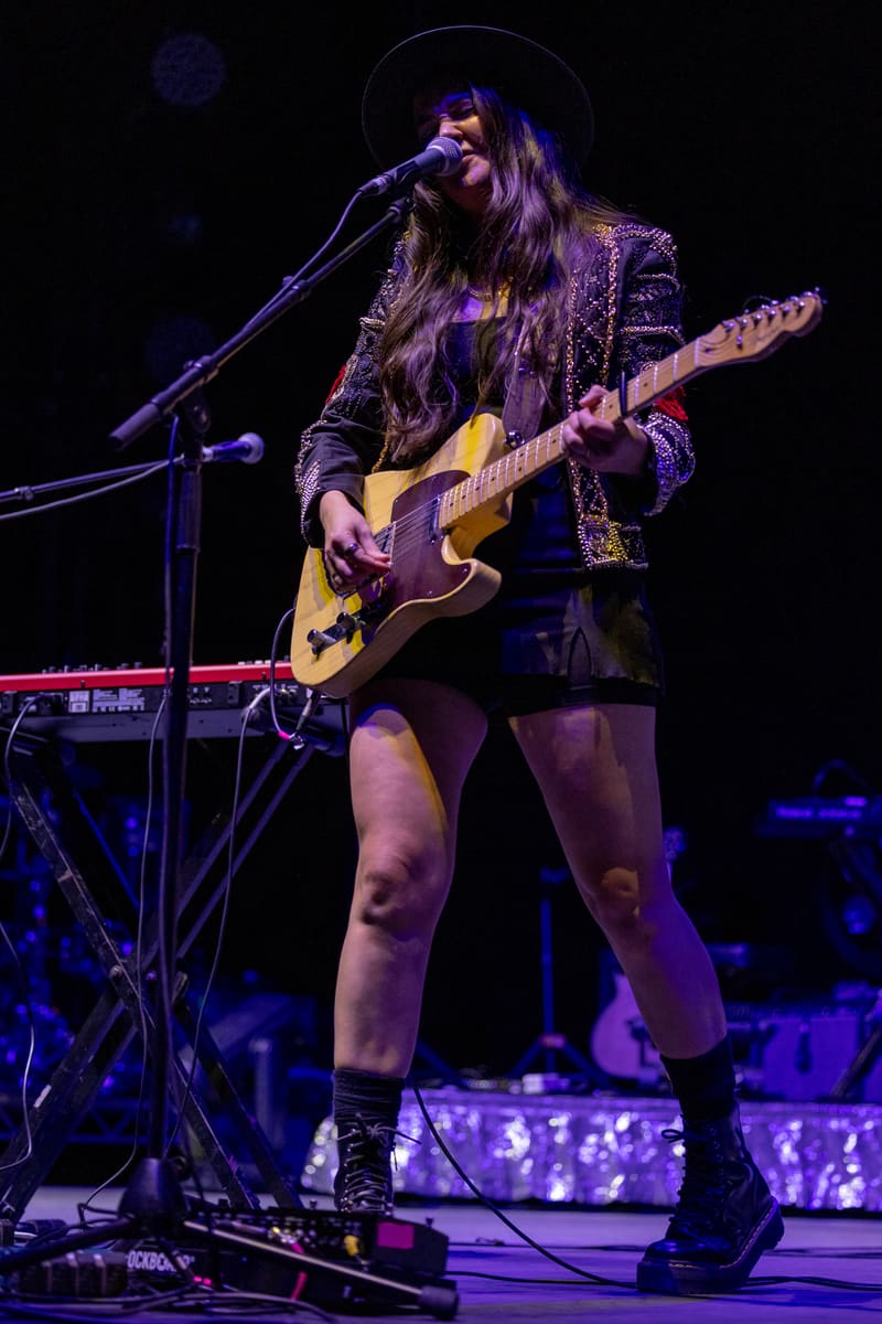 Performer singing and playing acoustic guitar on stage under purple spotlighting during The Corrs 2023 Australian Tour.