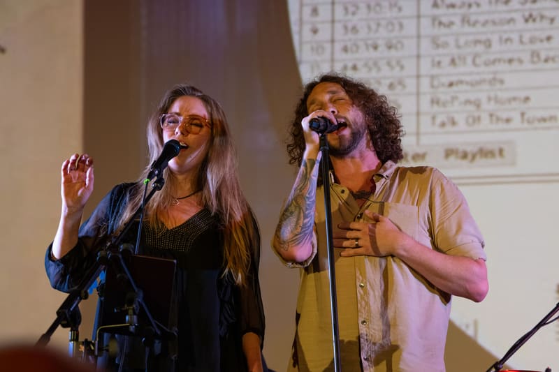 Two performers singing into microphones during a tribute performance at Gallery Five.