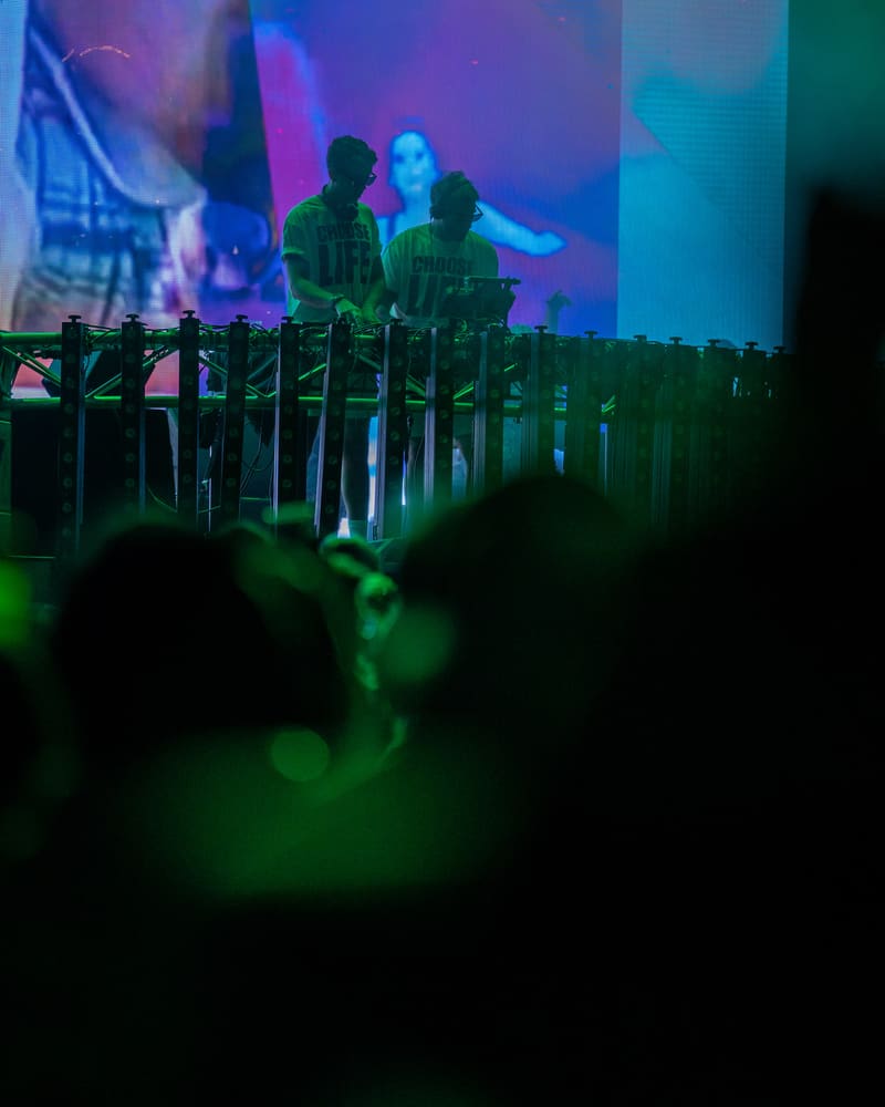 DJ performing at Harvest Rock Festival 2023 behind illuminated decks with coloured stage lighting and crowd silhouettes.