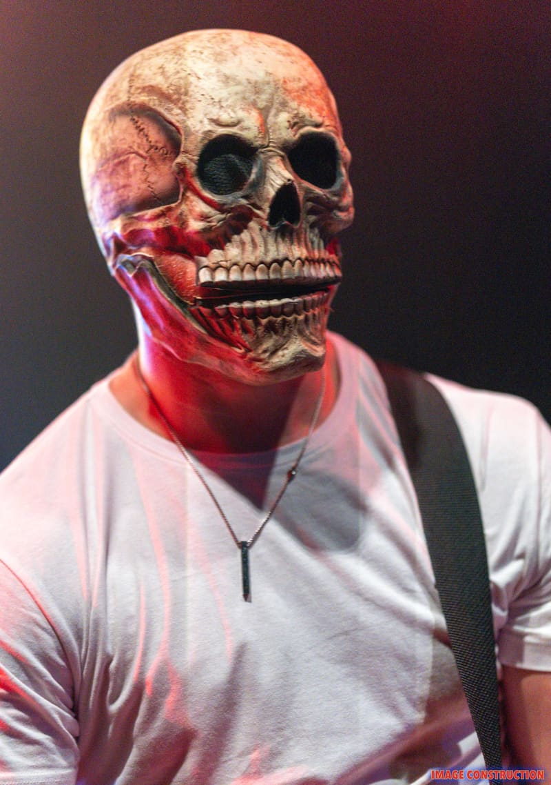Figure wearing oversized skull mask with red lighting effect and white t-shirt against dark background.
