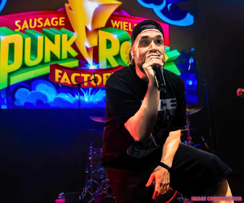 Performer singing into microphone against vibrant neon Punk Rock Factory signage backdrop.