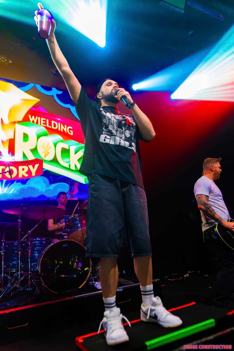 Singer in black shirt with fist raised, performing under bright blue and red stage lights at a rock venue.