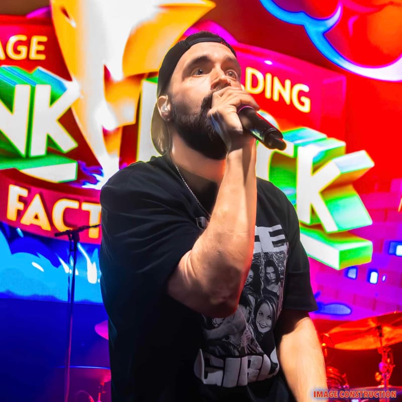 Bearded performer singing into microphone against vibrant neon signage at Punk Rock Factory.