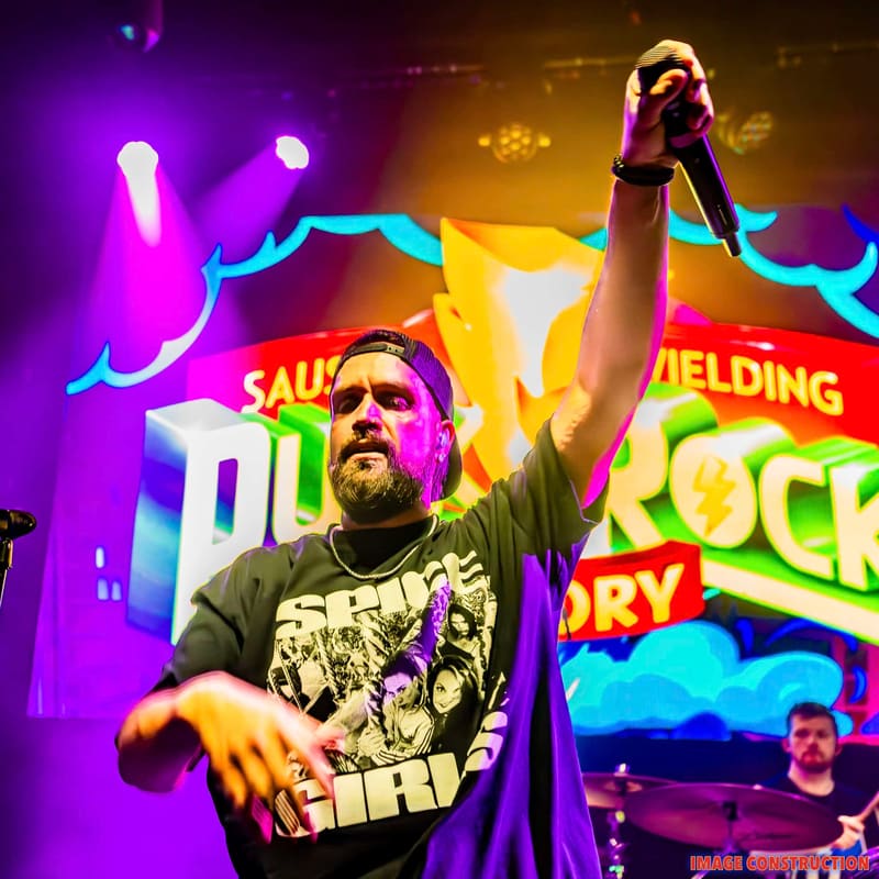 Performer raises fist on stage surrounded by neon purple and yellow lighting and bright signage.