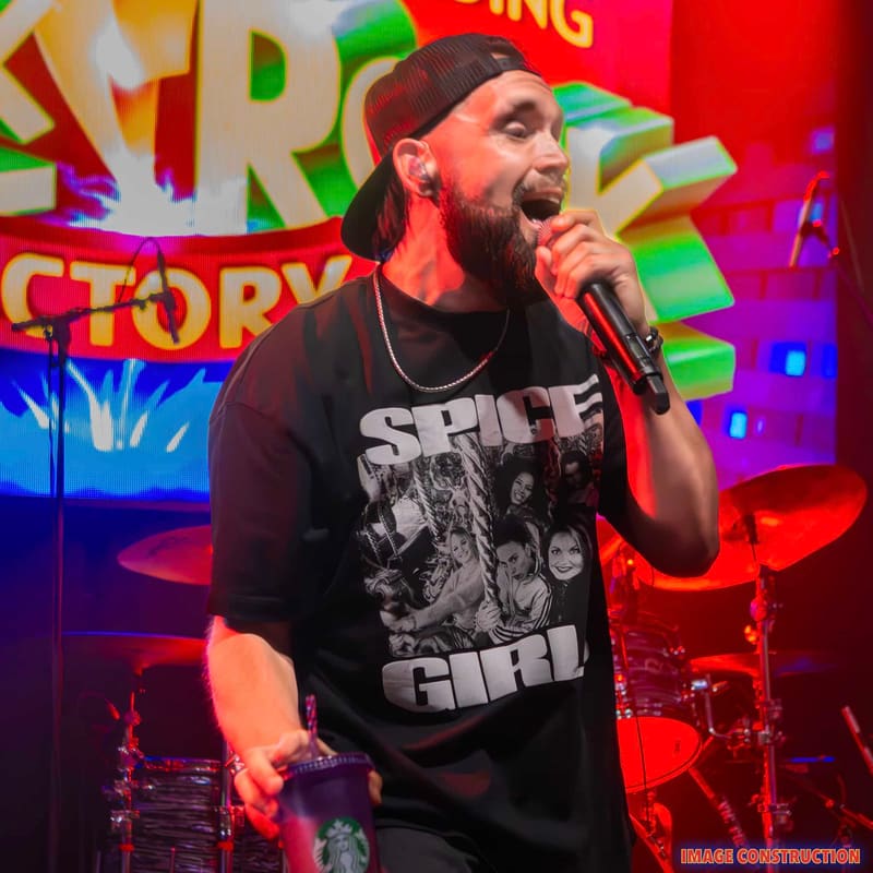 Bearded performer singing into a microphone against vibrant neon graffiti-style backdrop at Punk Rock Factory.