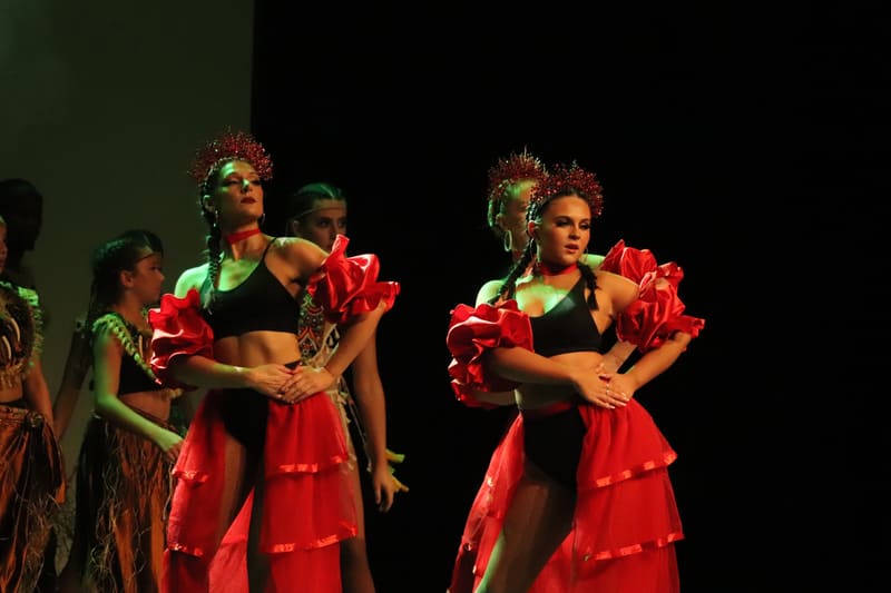 Dancers in vibrant red ruffled skirts and green crop tops perform together on stage at Viva Brazil.