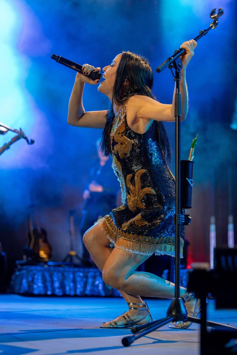 Singer performing at a microphone in a sequined dress under blue stage lighting during The Corrs Australian Tour 2023.