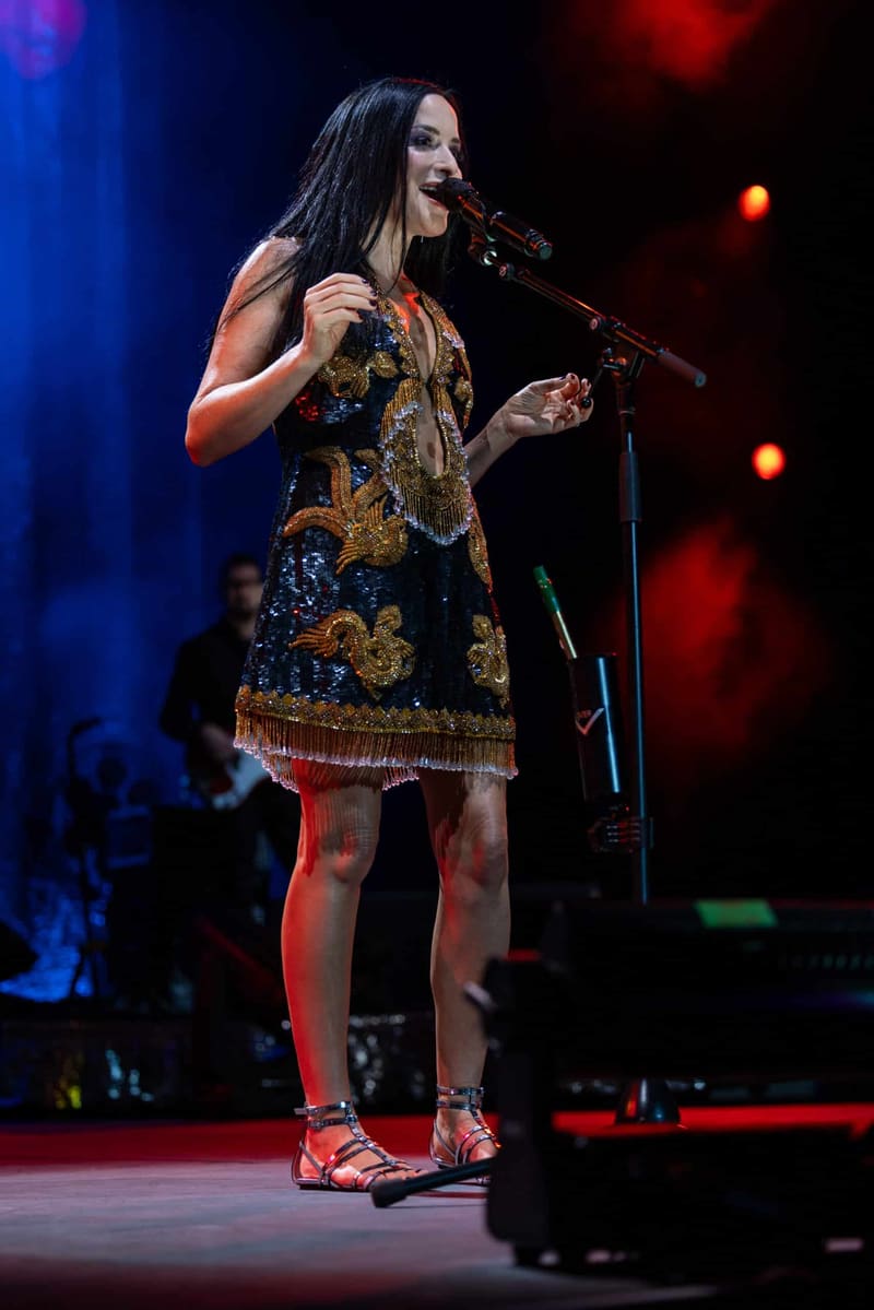 Singer in a gold-sequined dress performs at a microphone under red and blue stage lighting.