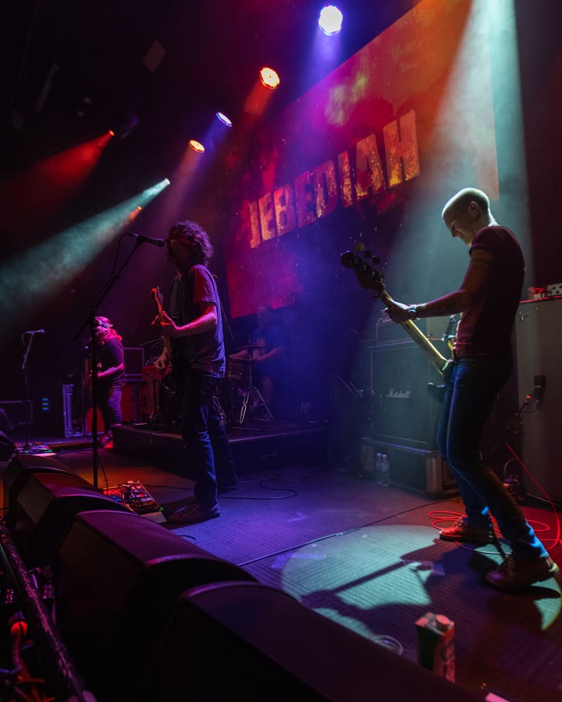 Band members perform on stage bathed in purple and red lighting during Jebediah's Gum Up The Bearings tour.