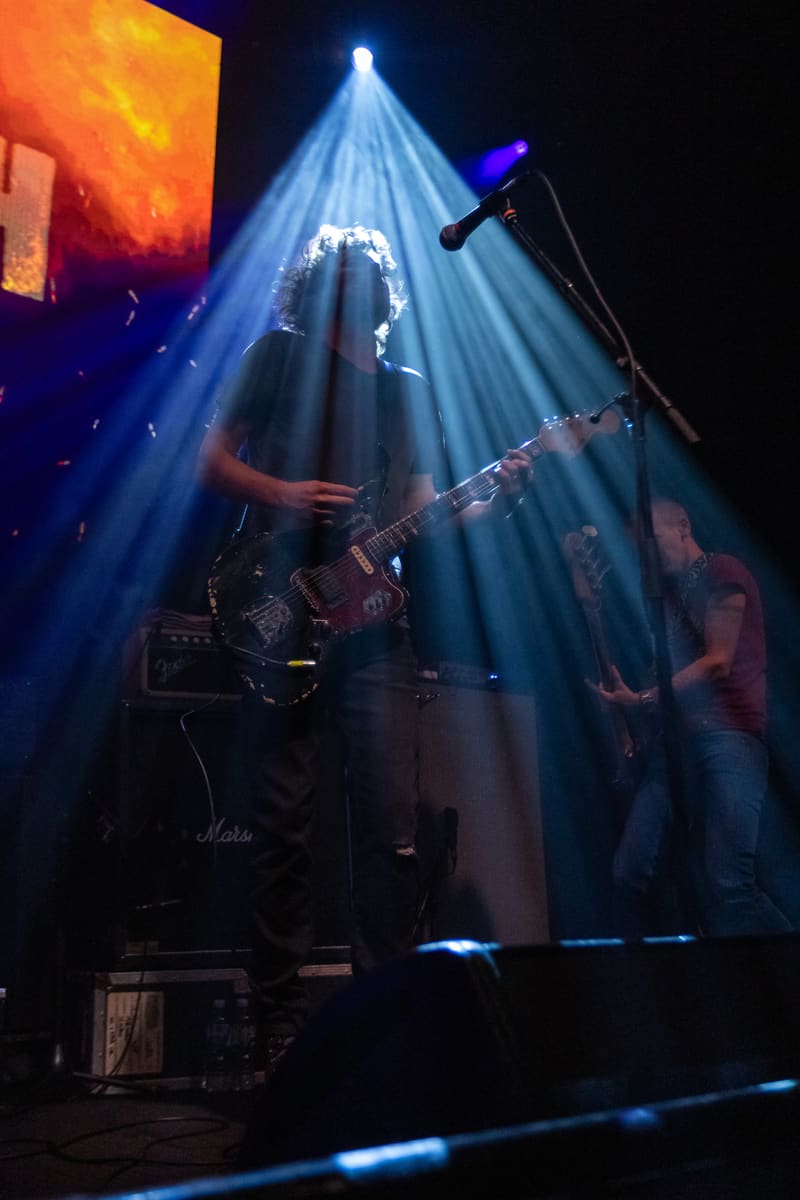 Guitarist silhouetted in dramatic blue spotlight beams during a Jebediah concert performance.