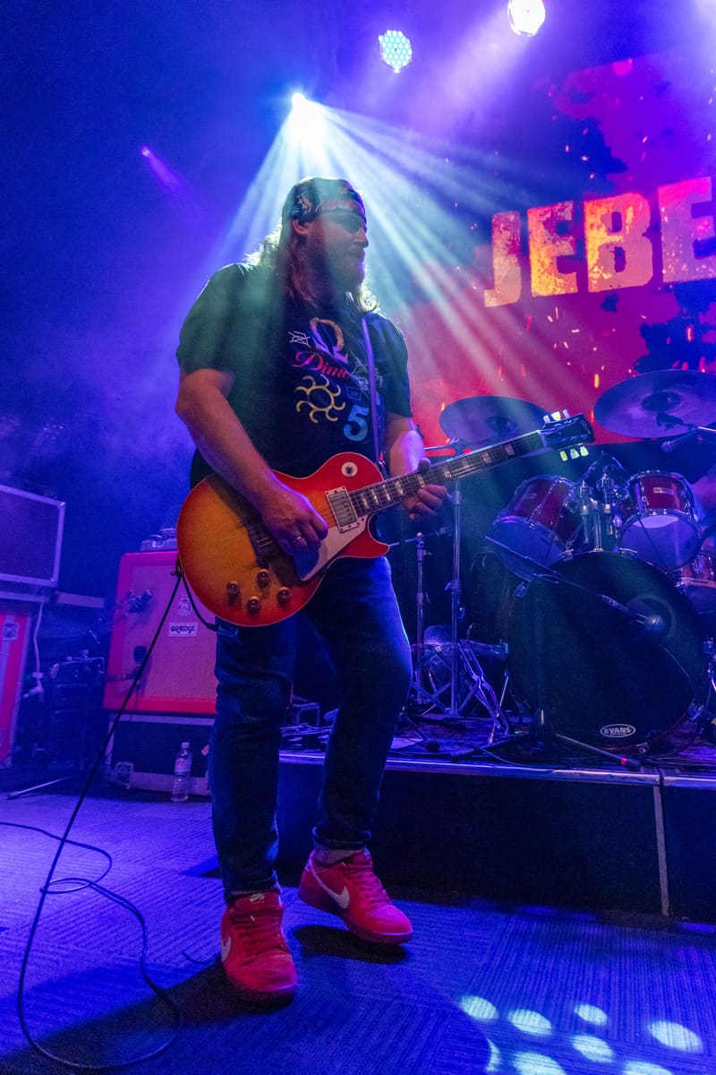 Guitarist performs with a sunburst electric guitar under purple and blue stage lighting during Jebediah's 2023 tour.