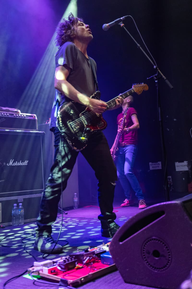 Guitarist performs at microphone during Jebediah's Gum Up The Bearings 2023 tour, bathed in purple stage lighting.