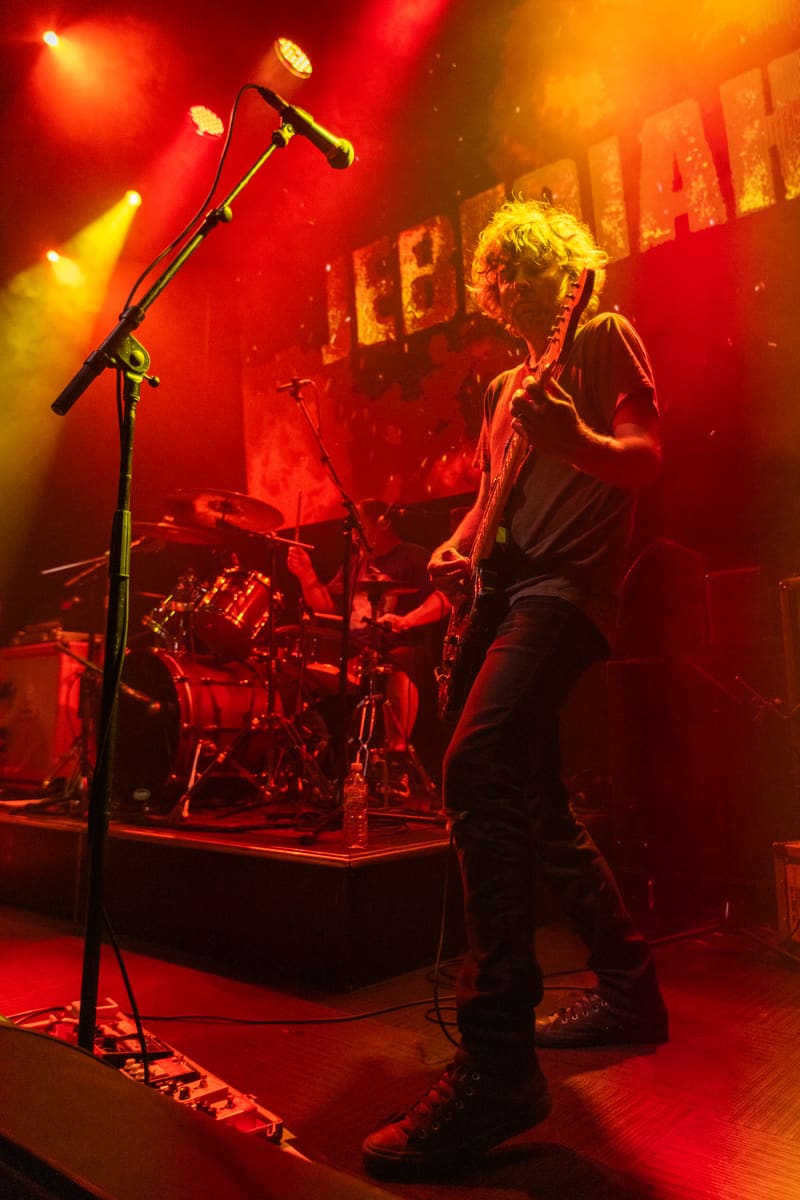 Musician performs on stage bathed in red and orange stage lights during Jebediah's Gum Up The Bearings 2023 Tour.