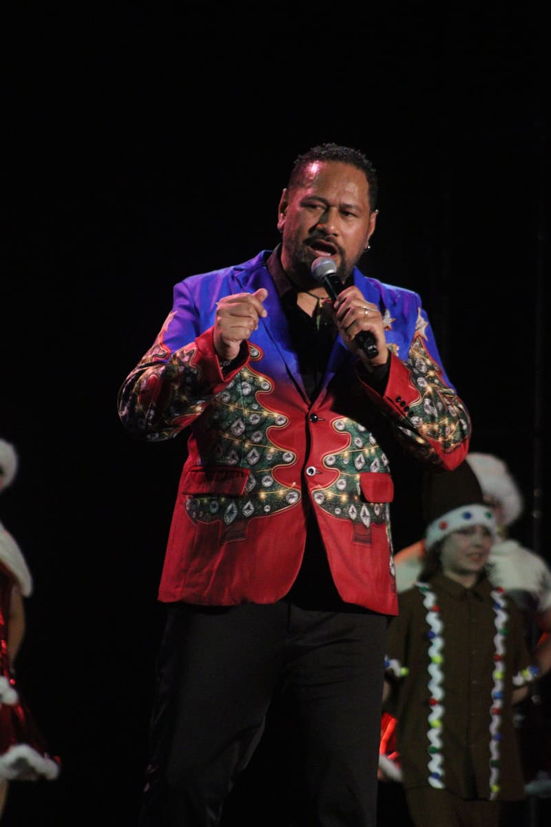 Male performer in a vibrant red and blue embroidered jacket singing at Adelaide Carols By Candlelight.